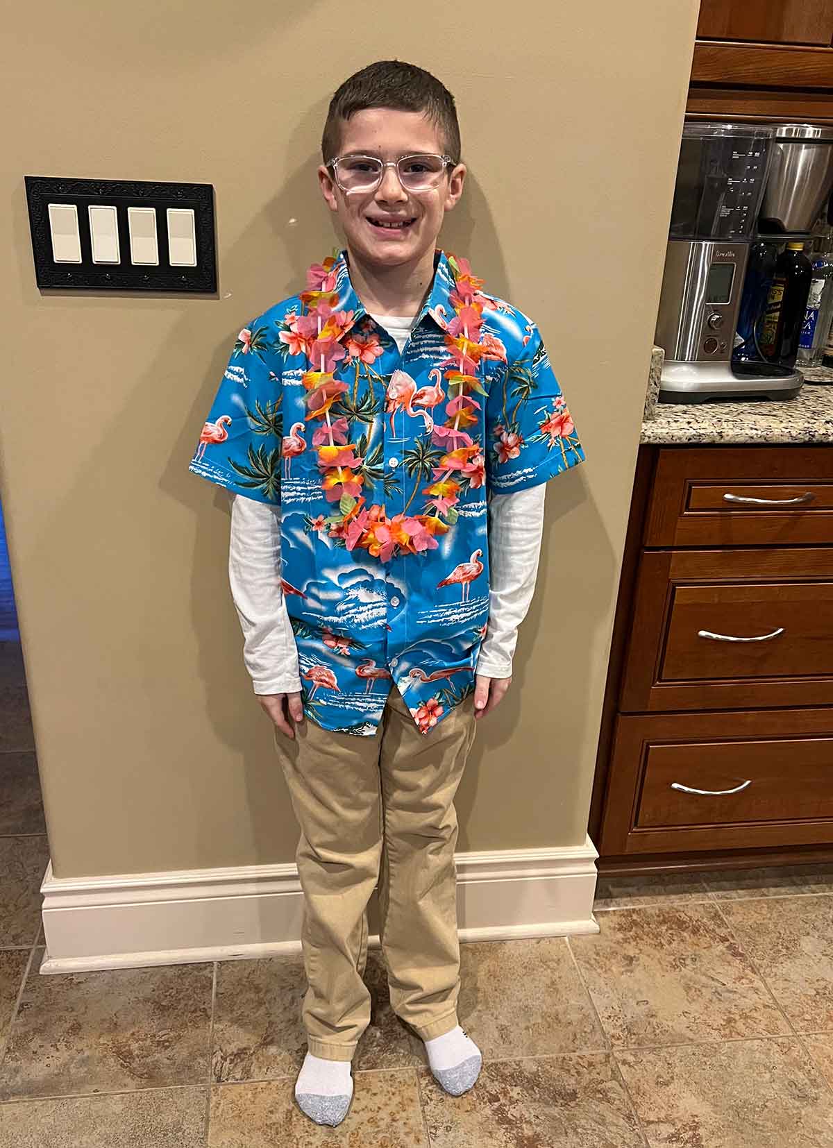 Boy wearing khaki pants, a Hawaaian shirt, and lei.