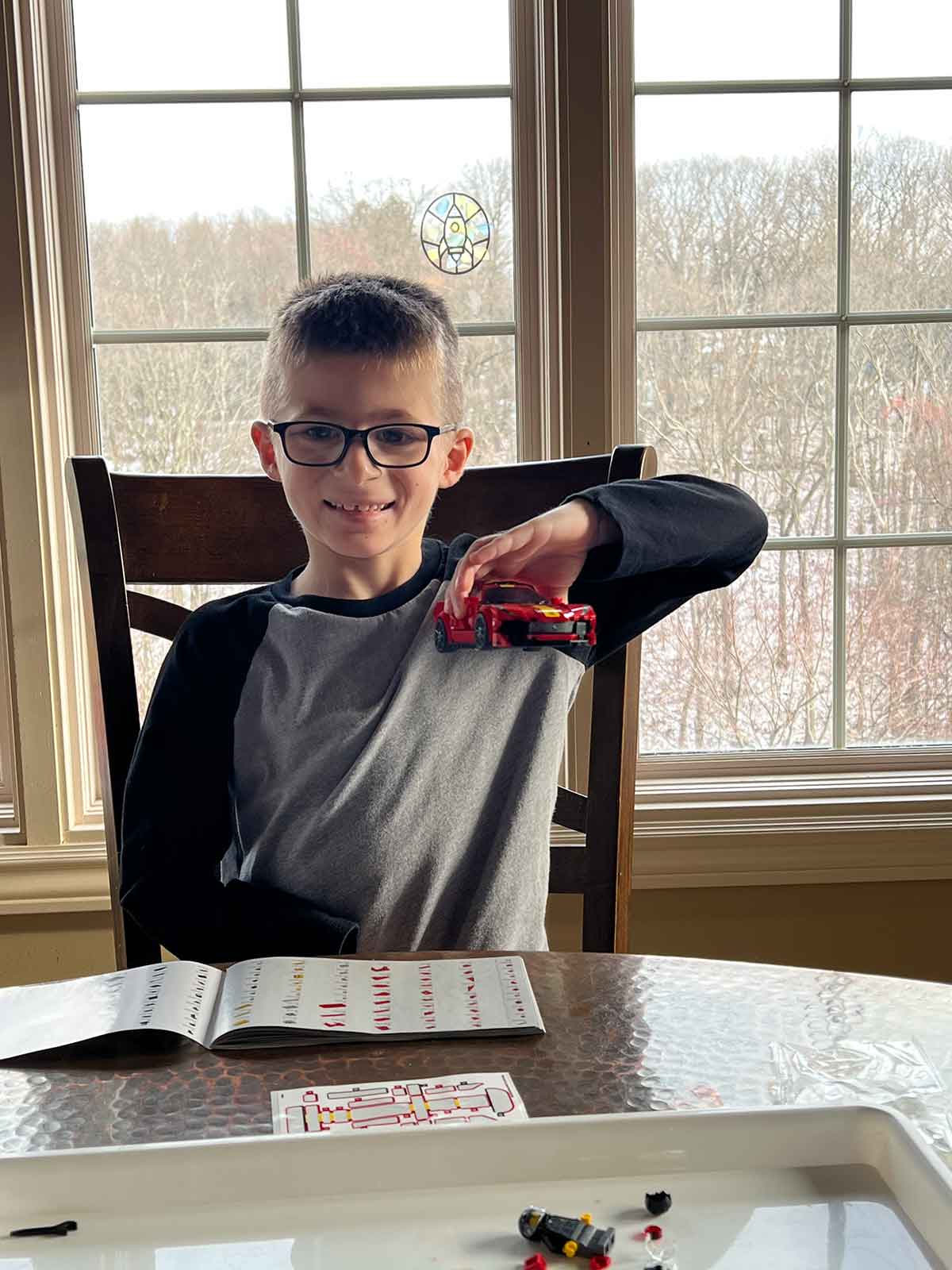 Little boy holding up a Lego car that he built.