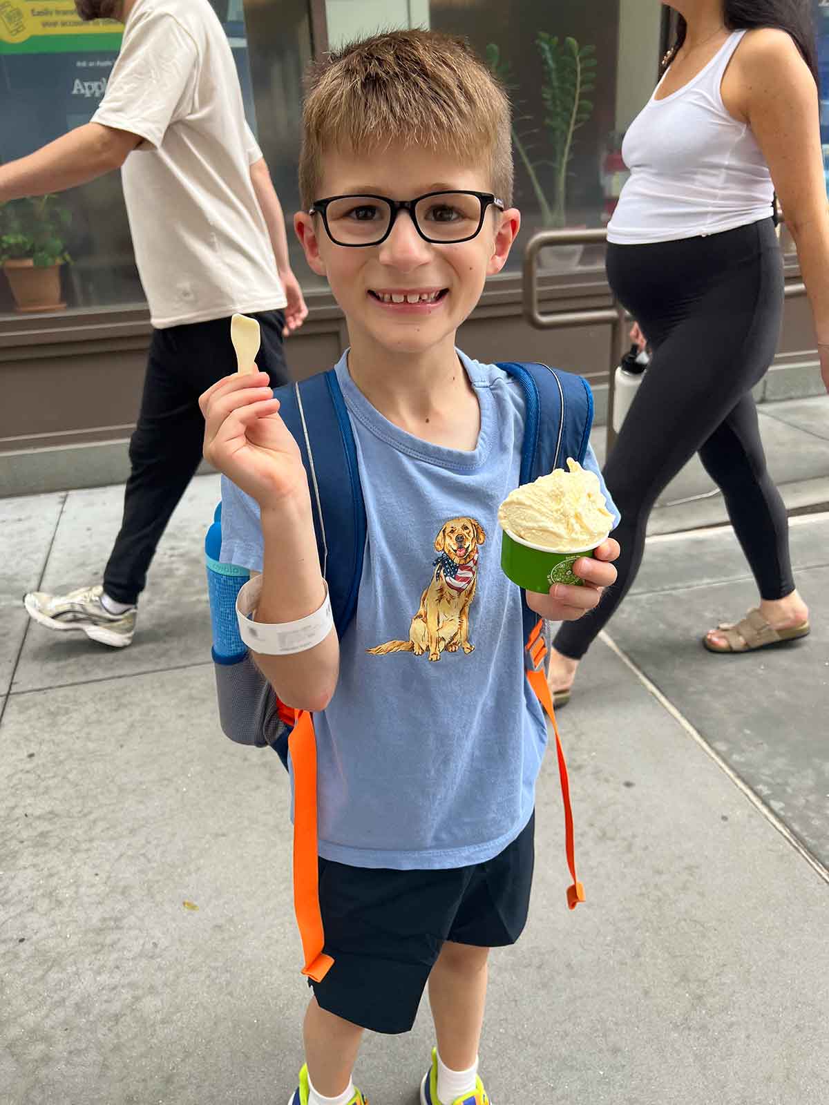Little boy standing on a city street eating a cup of gelato.