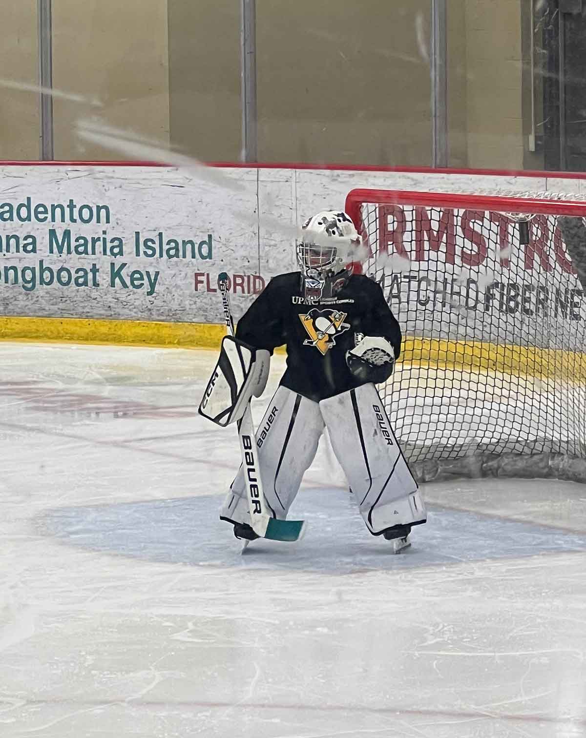 Little boy standing in front of a net playing goalie in an ice hockey game.