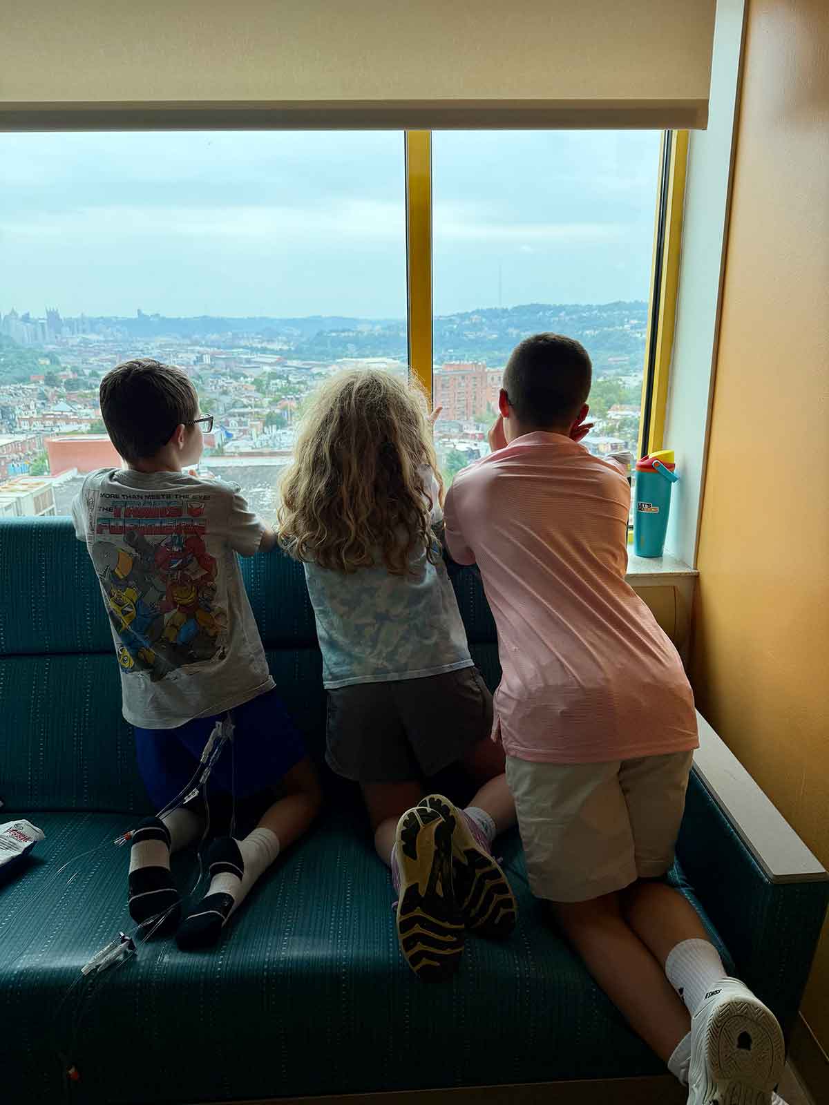 Three kids looking out of a hospital window together.