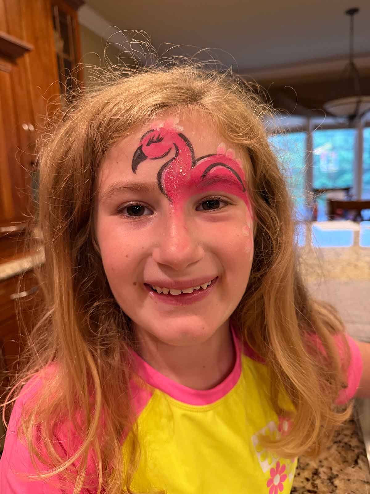 Little girl with her face painted with a flamingo on it.