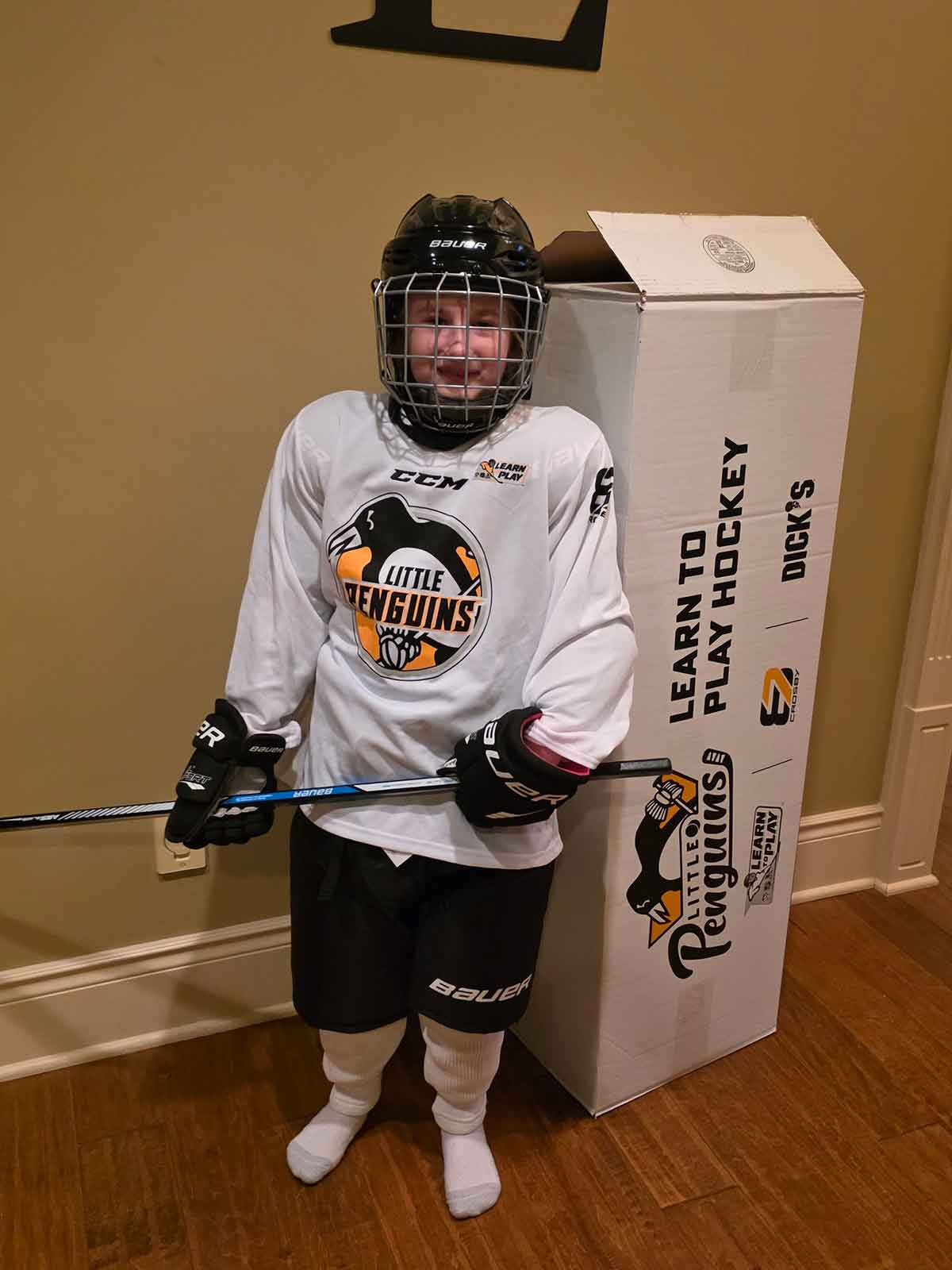 Girl wearing hockey equipment standing next to a large box.