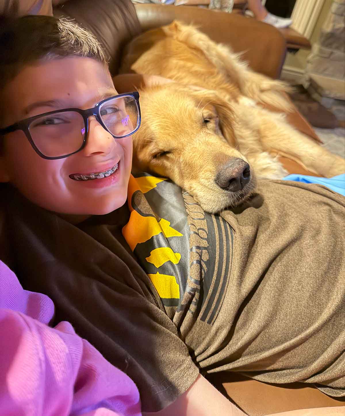 Boy snuggling on a couch with a sleeping dog.