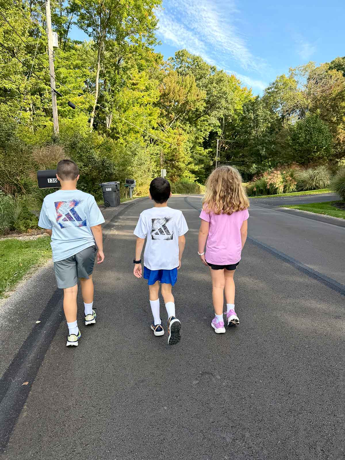 Three kids walking down a road surrounded by trees.
